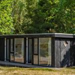 Moderne Holzhütte mit großem Glasfenster und Terrasse im Wald
