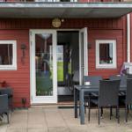 Roter Holzhaus-Eingang mit Terrasse, Tisch, Stühlen und offener Tür.