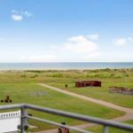 Rote Häuser, grünes Gras und Meer im Hintergrund. Picknicktische und Spielgeräte sind sichtbar.