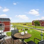 Terrasse mit Tisch und Stühlen. Blick auf grünes Gras und rote Häuser. Horizont über dem Meer.