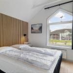 Schlafzimmer mit Holzwand, großem Fenster und Bett mit weißer Bettwäsche.