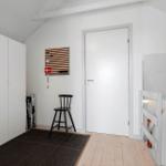 Raum mit weißen Wänden, Holzboden, Schrank und Stuhl. Tür und Treppe sind ebenfalls weiß.