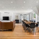 Großes Wohn- und Esszimmer mit braunem Sofa, Holzboden und langem Esstisch mit Stühlen.