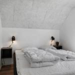 Schlafzimmer mit Doppelbett, weißen Wänden und schrägen Deckenpaneelen.