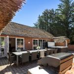 Terrasse mit Esstisch, Grill und Whirlpool. Roter Backsteinbau mit Strohdach und Bäumen im Hintergrund.