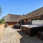 Terrasse mit Whirlpool, Grill und Tisch. Holzhaus mit Strohdach und Ziegelmauer.