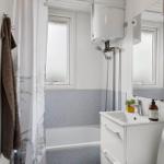Badezimmer mit Dusche, Waschbecken und Spiegel. Wandfarbe weiß und grau.