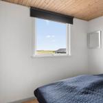 Schlafzimmer mit Bett, Fenster und Holzdecke. Draußen ist Feld und Himmel sichtbar.