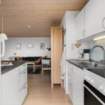 Küche mit weißen Schränken und Arbeitsfläche. Im Hintergrund ist ein Wohnzimmer mit Sofa und Tisch zu sehen.
