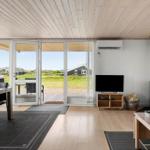 Wohn- und Essbereich mit Holzboden, TV, Kaminofen und Terrasse mit Blick auf Grasland.