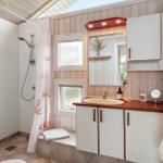 Badezimmer mit Dusche, Waschbecken und Spiegelschrank. Holzwand und Dachfenster.