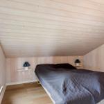 Schlafzimmer mit Holzwänden, Bett und Fenster. Zwei Nachttische mit Lampen.