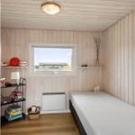 Ein Schlafzimmer mit Holzwand, Bett, Fenster und Regal mit Spielen.