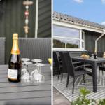 Außenbereich mit Tisch, Stühlen und Champagnerflasche. Haus mit dunkler Fassade und Terrasse.