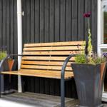 Holzbank mit zwei Pflanzenkästen auf einer Terrasse vor einem Haus mit dunklem Holzverkleidung.