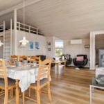 Großes Wohnzimmer mit Essbereich, Holzdecke und -boden, schwarze Sessel und Tisch mit Tischdecke.