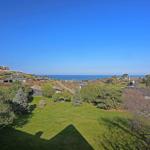 Green lawn with trees and ocean view under blue sky.