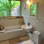 Bathroom with bathtub, sink, and toilet. Window with view of green trees.