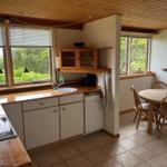 Kitchen with dining area, wooden table, chairs, and windows with green view.