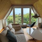 Living room with wooden ceiling, sofa, table, and balcony with view of greenery and sea.