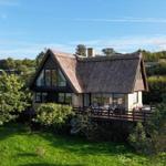 House with thatched roof and wooden terrace in green surroundings