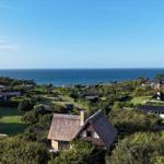 House with thatched roof, surrounded by greenery and trees, view of the sea.