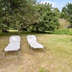 Two white lounge chairs are on a lawn under trees.