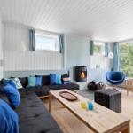Living room with sofa, fireplace, and seating. Wooden floor and large windows.