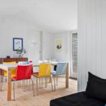 Dining room with colorful chairs and wooden floor. Kitchen and bedroom in the background.