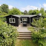 Black wooden house with terrace, garden, and trees in the background.