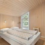 Schlafzimmer mit Holzwandverkleidung, Bett, Fenster und Kleiderschrank.