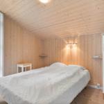 Schlafzimmer mit Holzwand und -decke, großes Fenster, Bett mit weißer Decke, Schrank und Wandlampe.
