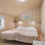 Schlafzimmer mit Holzwand, Bett, Fenster und Stuhl.