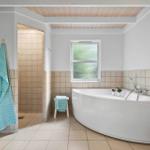 Bad mit freistehender Badewanne, Dusche und Fenster. Holzdecke und Fliesenwand.