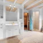 Badezimmer mit Dusche, Badewanne und Sauna. Weiße Einbauschränke und Holzdecke.