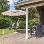 Terrasse mit Tisch, Stühlen und Sonnenschirm. Hintergrund: grüner Garten und Holzwand.