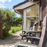 Terrasse mit Tisch, Stühlen und Thermoflasche. Hintergrund: Grünflächen und Holzhauswand.
