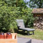 Liegestuhl im Garten neben Holzstapel und grüner Vegetation.