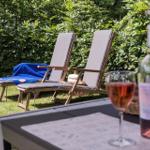 Zwei Liegestühle mit blauer Decke stehen im Garten. Auf Tisch steht ein Glas und eine Flasche Rosé.