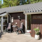 Haus mit Holzfassade, Terrasse mit zwei Stühlen und Tisch, Pflanze vor der Tür.