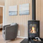 Wohnraum mit Kaminofen, Sessel und Blick in Schlafzimmer.