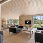 Wohn- und Essbereich mit Holzdecke, schwarzen Sofas und großen Fenstern.