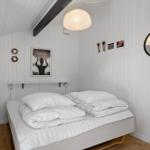 Schlafzimmer mit weißem Bett, Holzboden und weißen Wänden. Deckenbalken und Pendelleuchte.