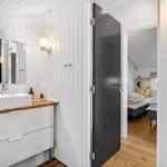 Badezimmer mit Waschtisch und Spiegel. Tür führt in Schlafzimmer mit Bett.