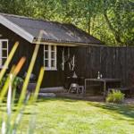 Hütte mit Garten, Grill und Tisch. Umgeben von Bäumen und Gras.