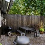Hinterhof mit Tisch, Bänken, Grill und Pflanzen an Holzhauswand.