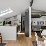 Wohnung mit Küche, Essbereich und Wohnzimmer. Holzboden, weiße Wände und Dachfenster.