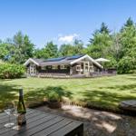 Holzhütte mit Terrasse, Garten und Sonnenkollektoren. Tisch mit Wein im Vordergrund.