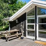 Hütte mit Holzterrasse, Picknicktisch und Glastür. Umgeben von Bäumen.