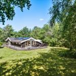 Ein Holzhaus mit Terrasse und Solaranlage auf grünem Grundstück umgeben von Bäumen.